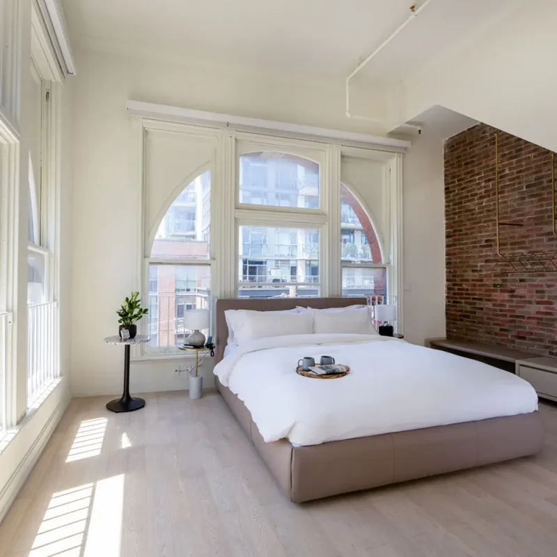 Gladstone House guest suite with King sized bed beside large, brightly lit windows and exposed brick wall