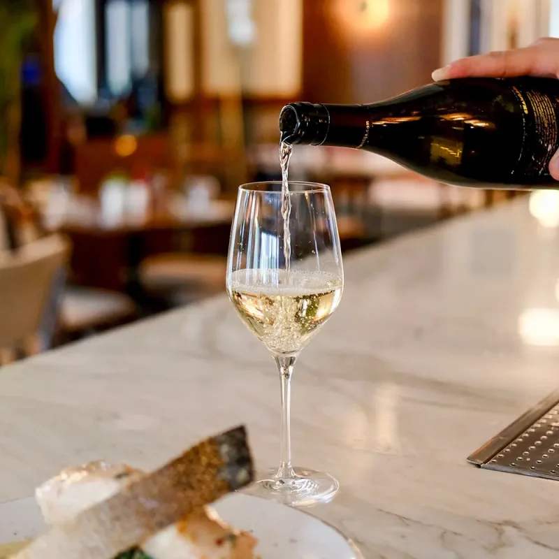 Glass of white wine being poured on Postmark hotel bar with crustini bread