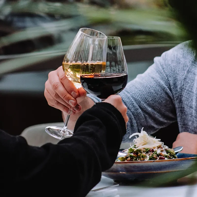 Postmark Hotel guests toasting 2 glasses of wine over salad dish
